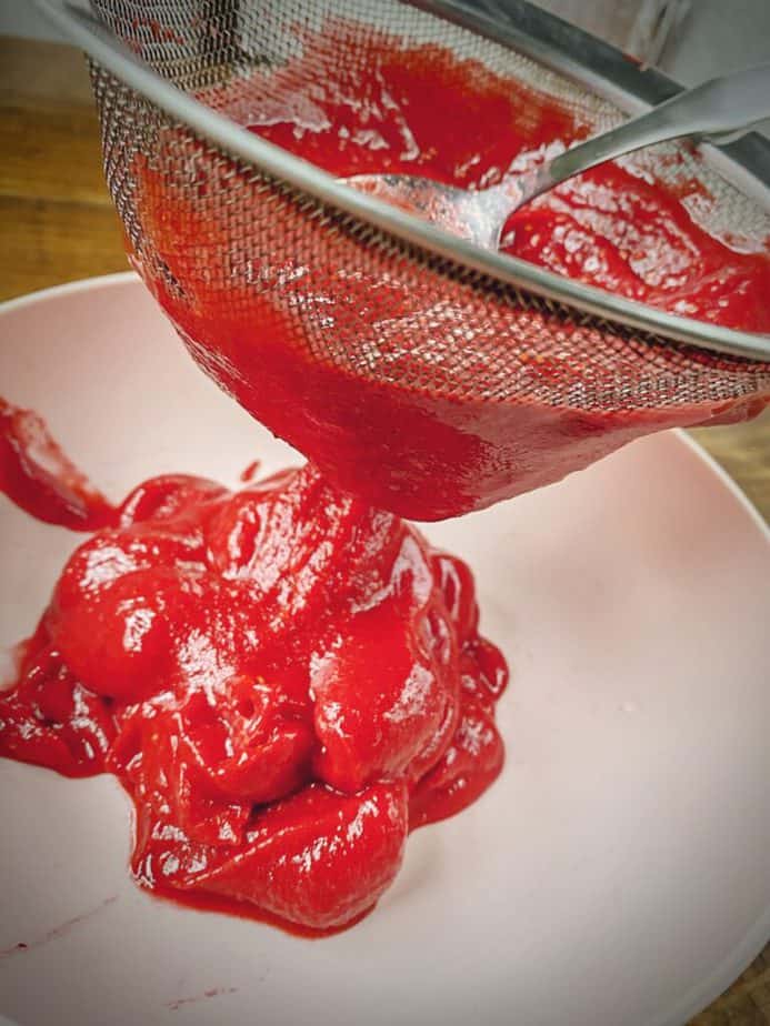 spoon pushing raspberry amaretto purée through a sieve to remove seeds for sauceamaretto pur