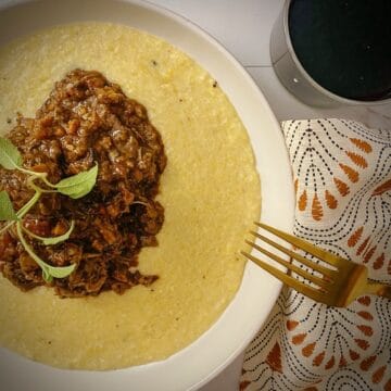 red wine braised short ribs over parmesan polenta in a white pasta bowl garnished with fresh sage.