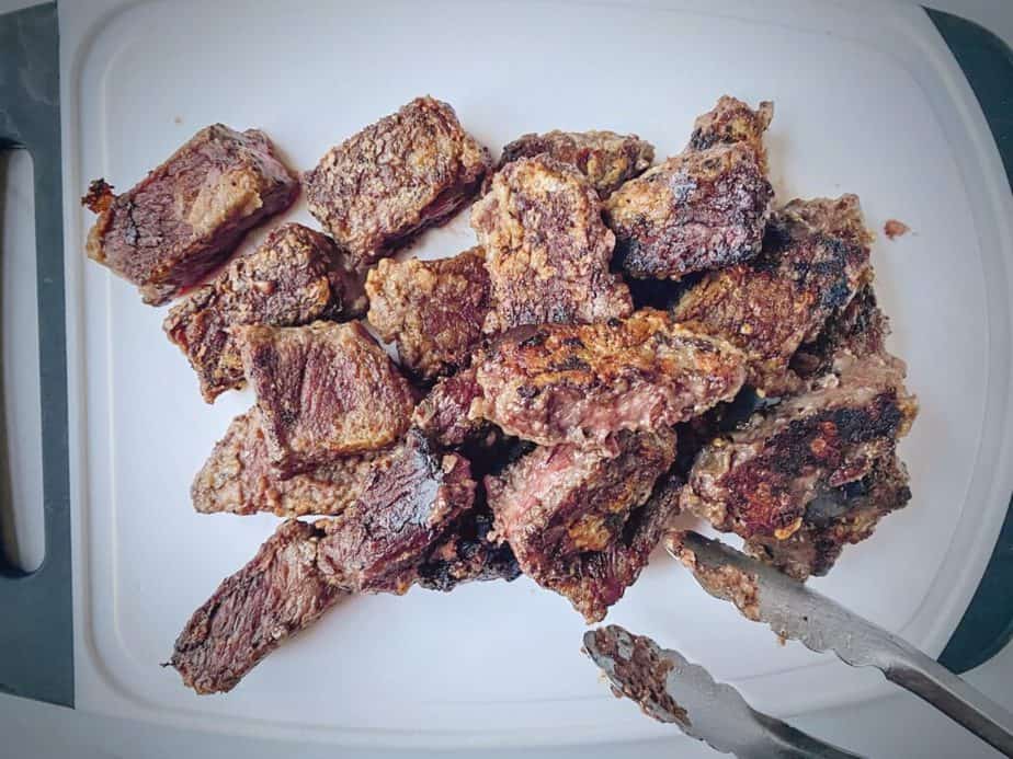 pile of browned short rib chunks on a cutting board with tongs