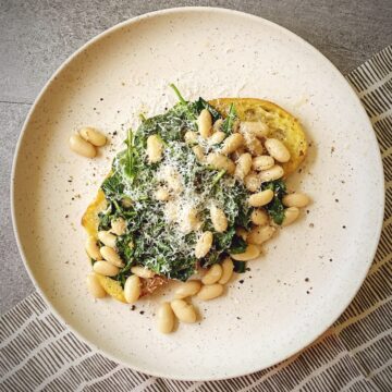 overhead shot of beans and greens on toast with parmesan topping on a natural plate.