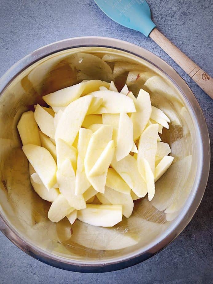 peeled and sliced apples in a silver mixing bowl