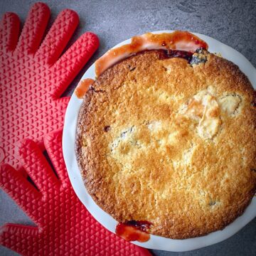 overhead shot of apple cherry easy fruit cobbler in a pie dish with red oven mitts to the side.