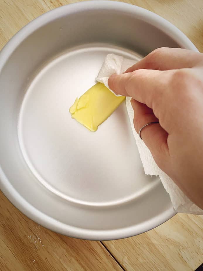 hand spreading butter in a cake tin using a paper towel