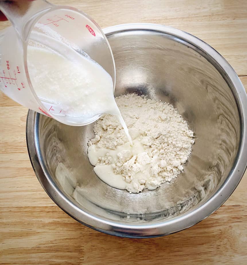 hand pouring buttermilk into a silver mixing bowl with biscuit mix