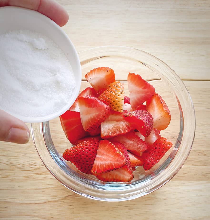 hand pouring sugar over sliced strawberries