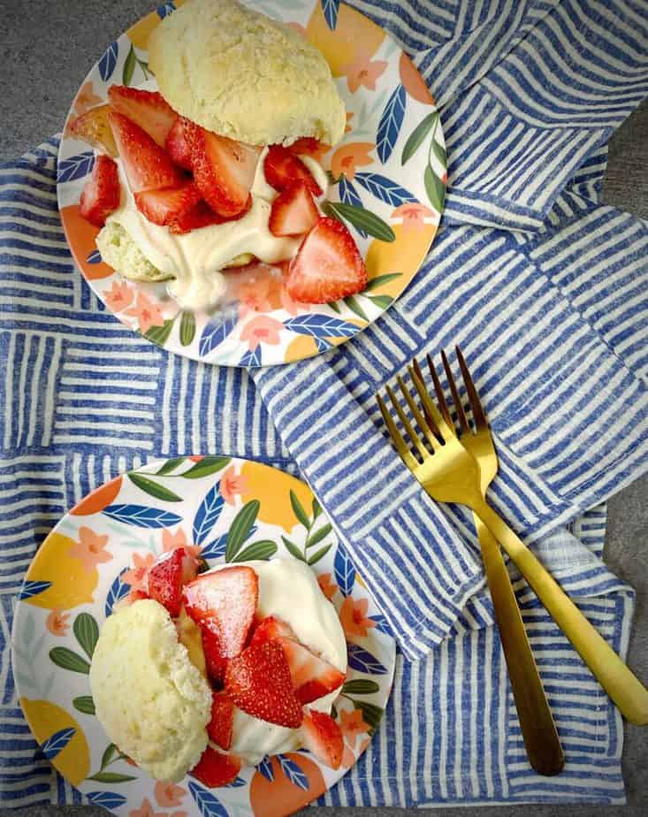 overhead shot of two small dessert plates with classic strawberry shortcake on a blue and white striped tea towel
