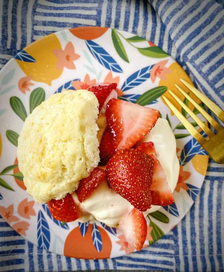 closeup overhead shot of classic biscuit strawberry shortcakes on a floral plate with a gold fork