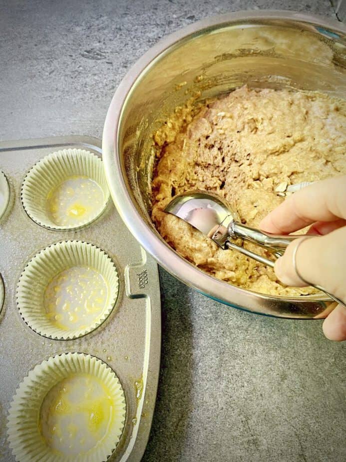 hand using a disher to scoop out muffin batter into tin