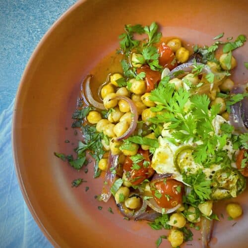 overhead shot of a portion of baked feta with chickpeas and tomatoes in a terracotta bowl