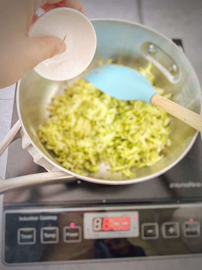 hand pouring in kosher salt into saucepan with grated zucchini