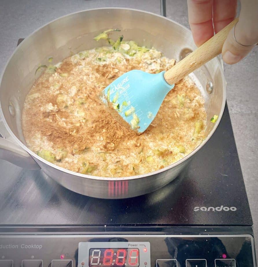 hand stirring zucchini oat mixture together in saucepan