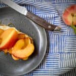 peach and ricotta tartine on a grey speckled plate with a wooden handled steak knife and a whole peach