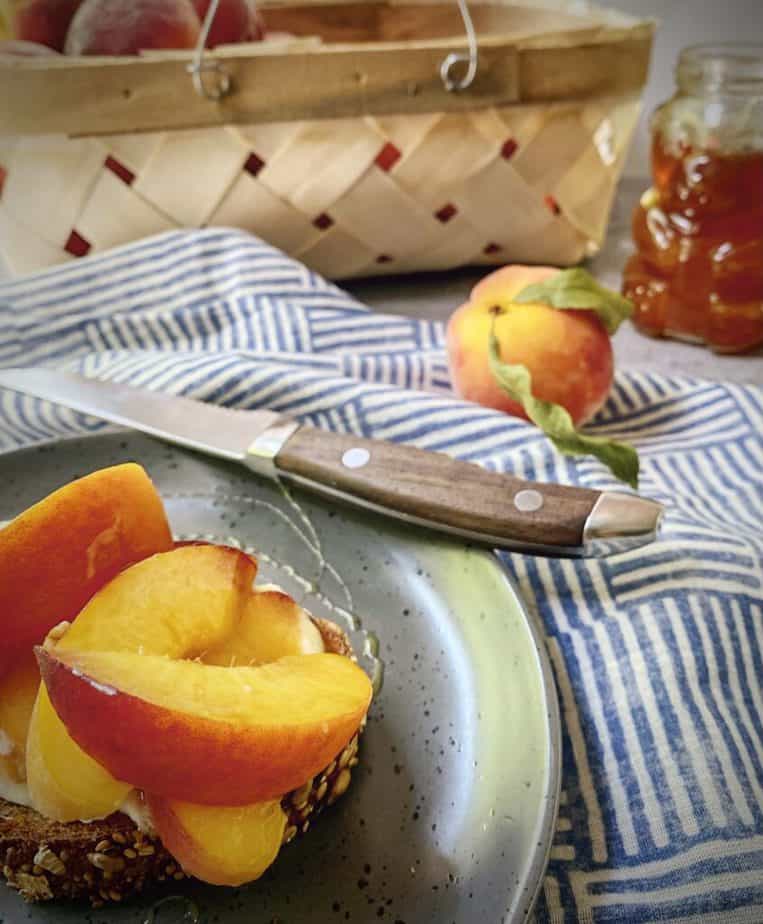 peach tartine picnic scape with a woven basket of peaches and a blue and white striped cloth