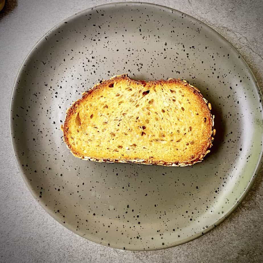 overhead shot of piece of multigrain toast on a grey speckled plate