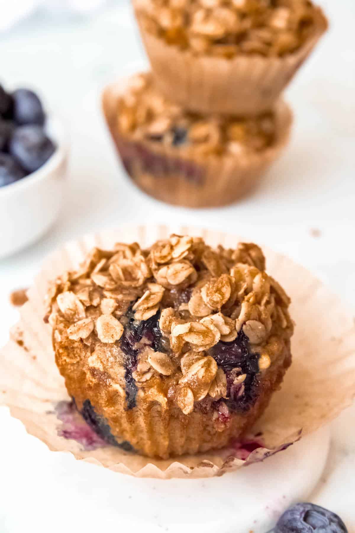closeup 45 degre angle shot of a single banana blueberry oatmeal muffin sitting atop the wrapper that has been pulled away.