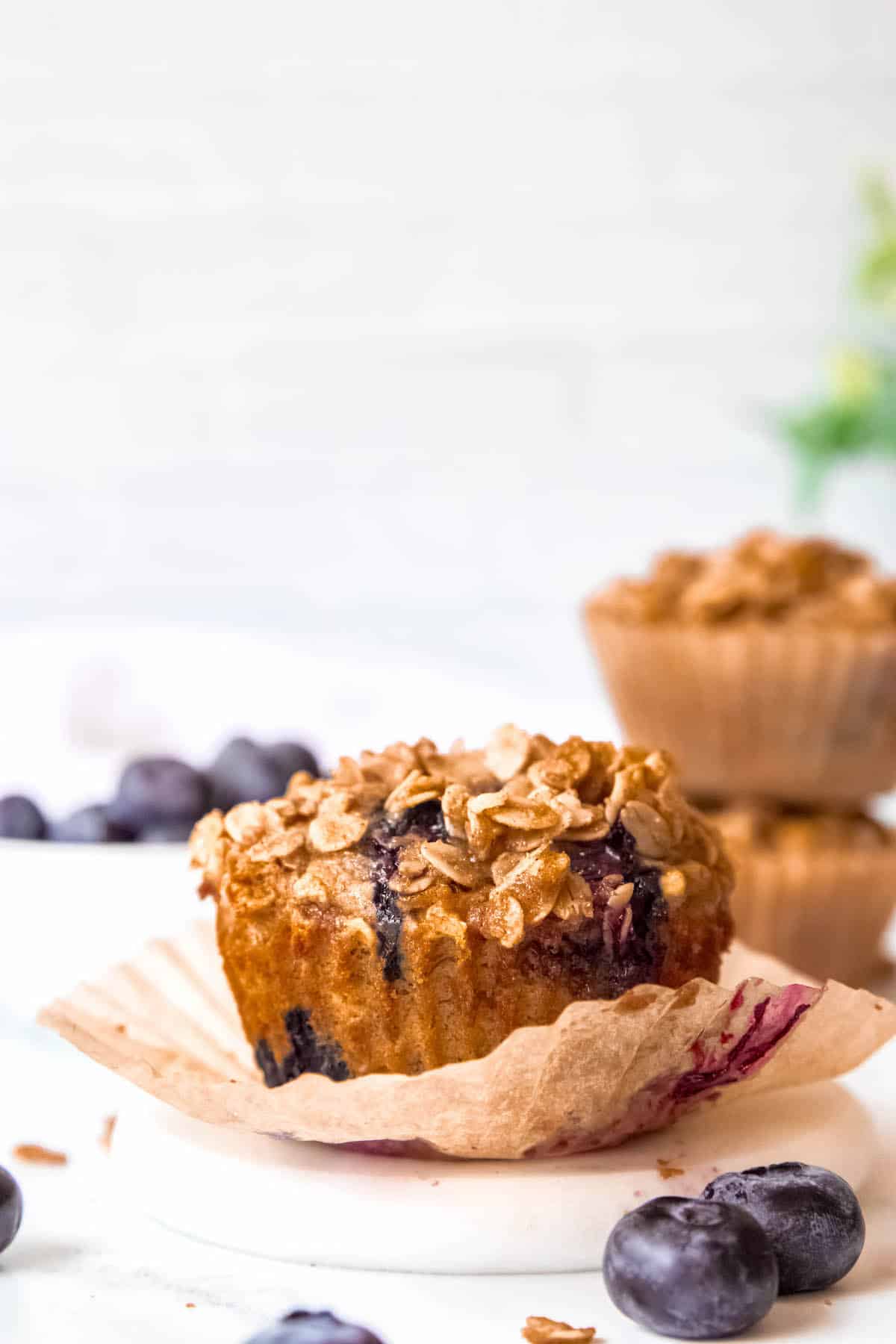 side on image of a banana blueberry oatmeal muffin with a bowl of blueberries.