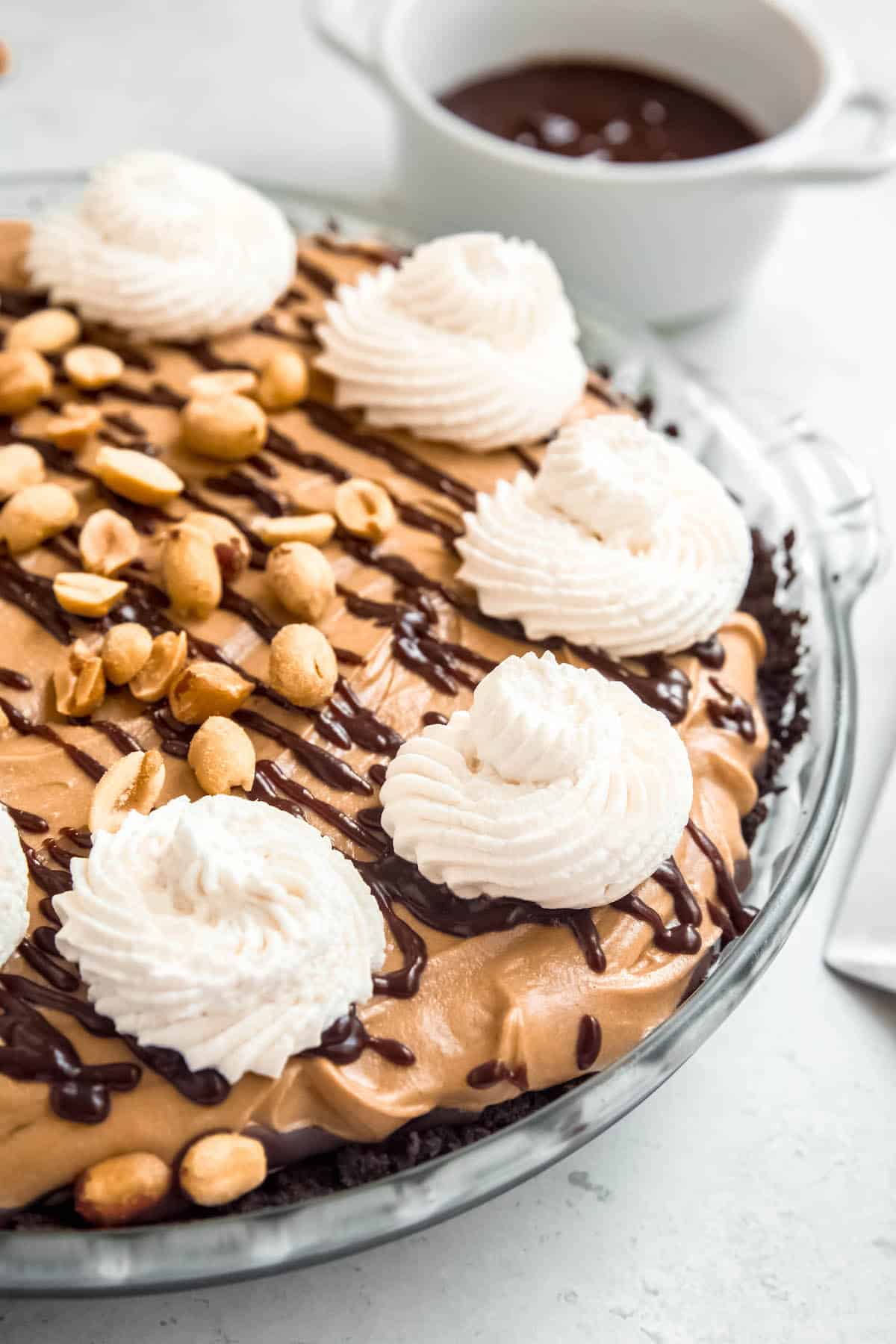45 degree angle shot of peanut butter pie with oreo crust, chocolate peanut butter ganache, freshly whipped cream, and roasted, salted peanuts.