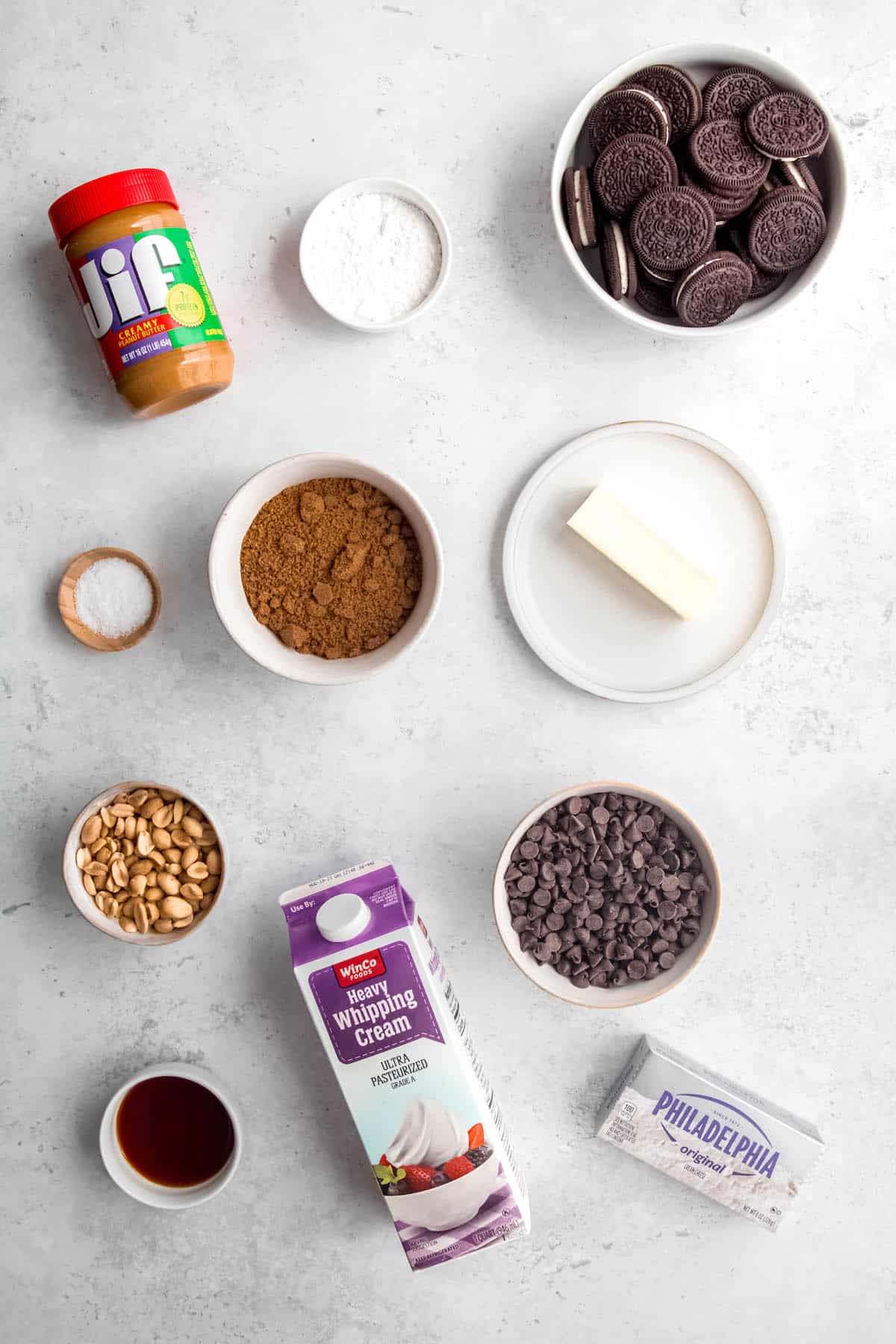 ingredients needed to make chocolate peanut butter pie with oreo crust and chocolate peanut butter ganache measured out into bowls on a white table.