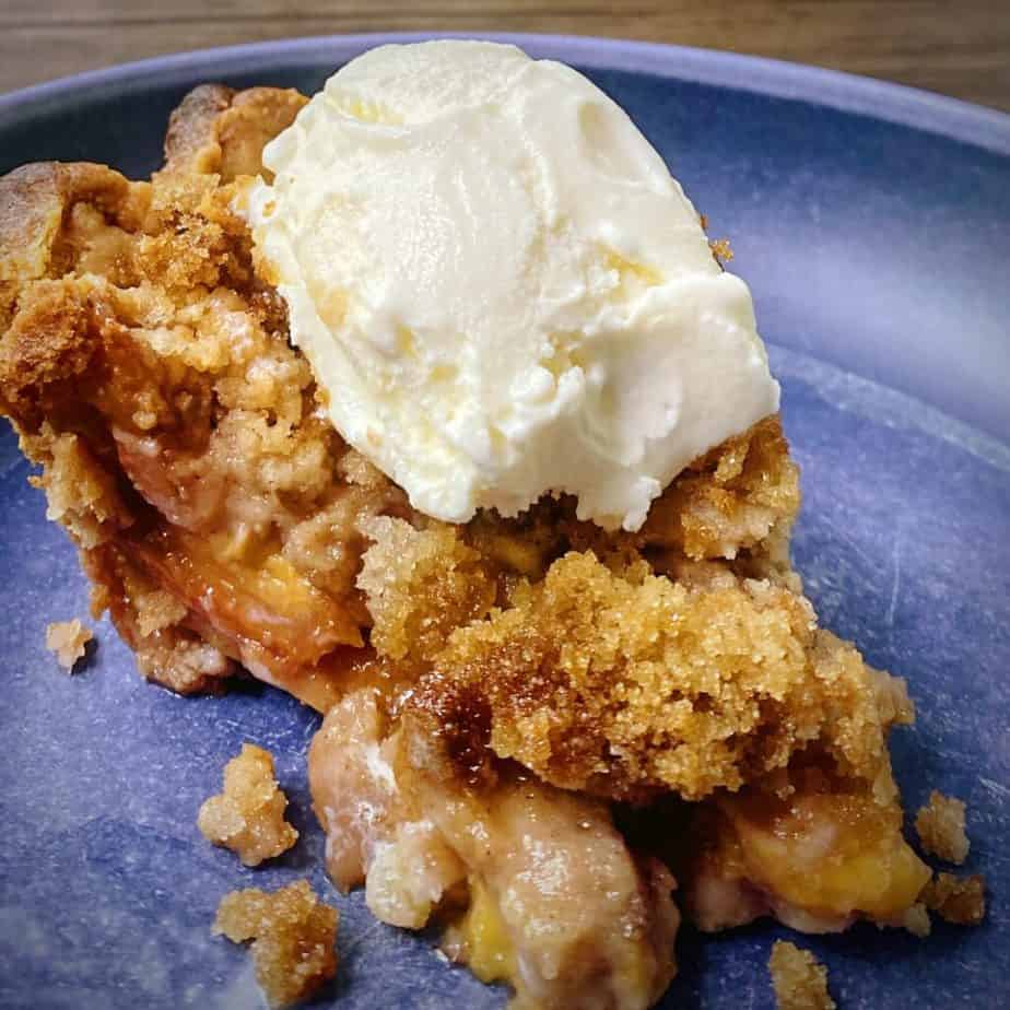 close up of a slice of peach crumble pie with ice cream to show texture