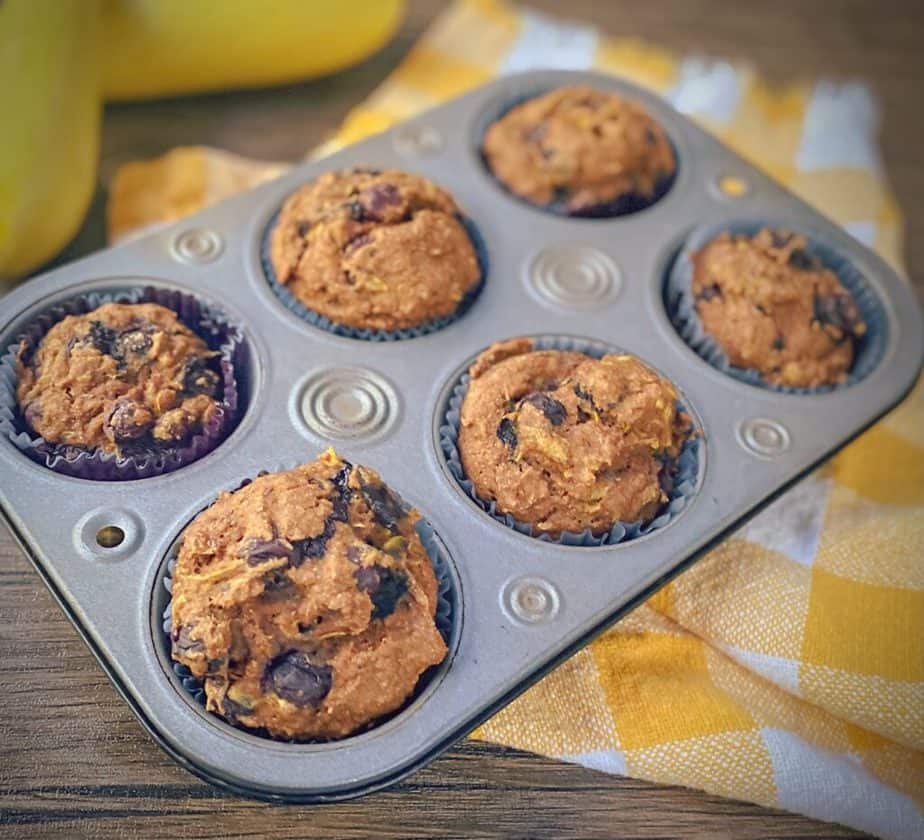 six blueberry summer squash muffins in a silver decorative tin with a yellow and white gingham dish towel