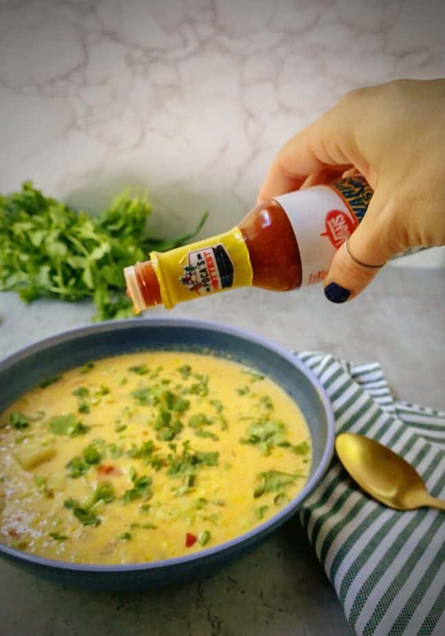 hand shaking a bottle of hot sauce over a bowl of easy corn chowder