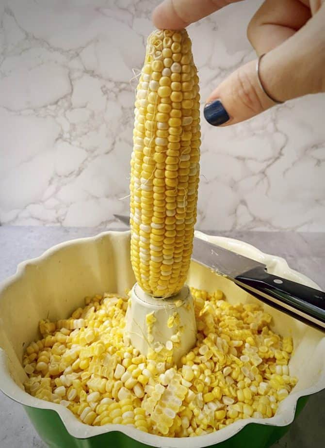 hand holding cob of corn on middle part of bundt pan for removing kernels