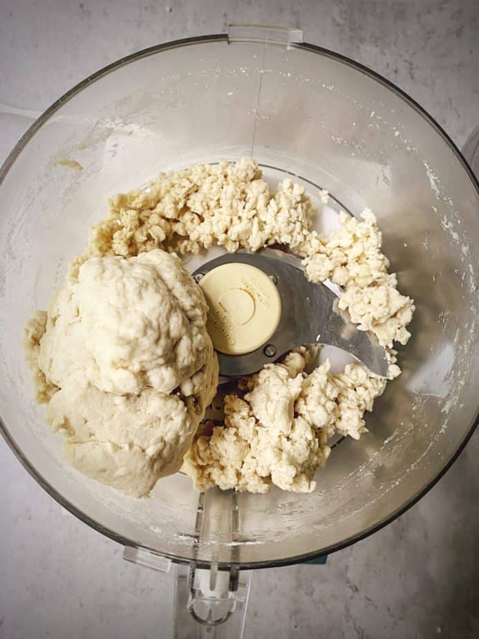pancake dough in the bowl of food processor, showing a big ball of dough with remaining dough clearly well enough integrated to stick together