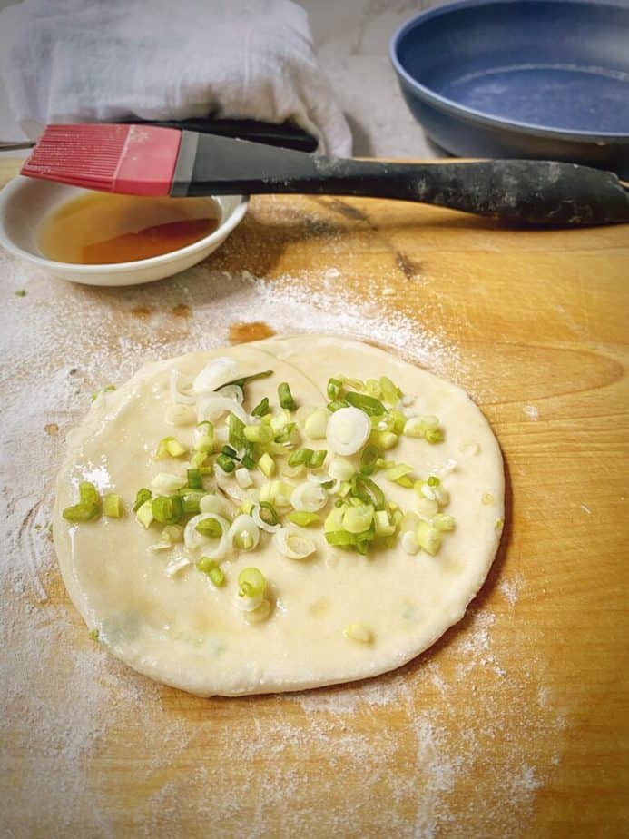 rolled out dough is brushed with oil again and scallions are sprinkled on top