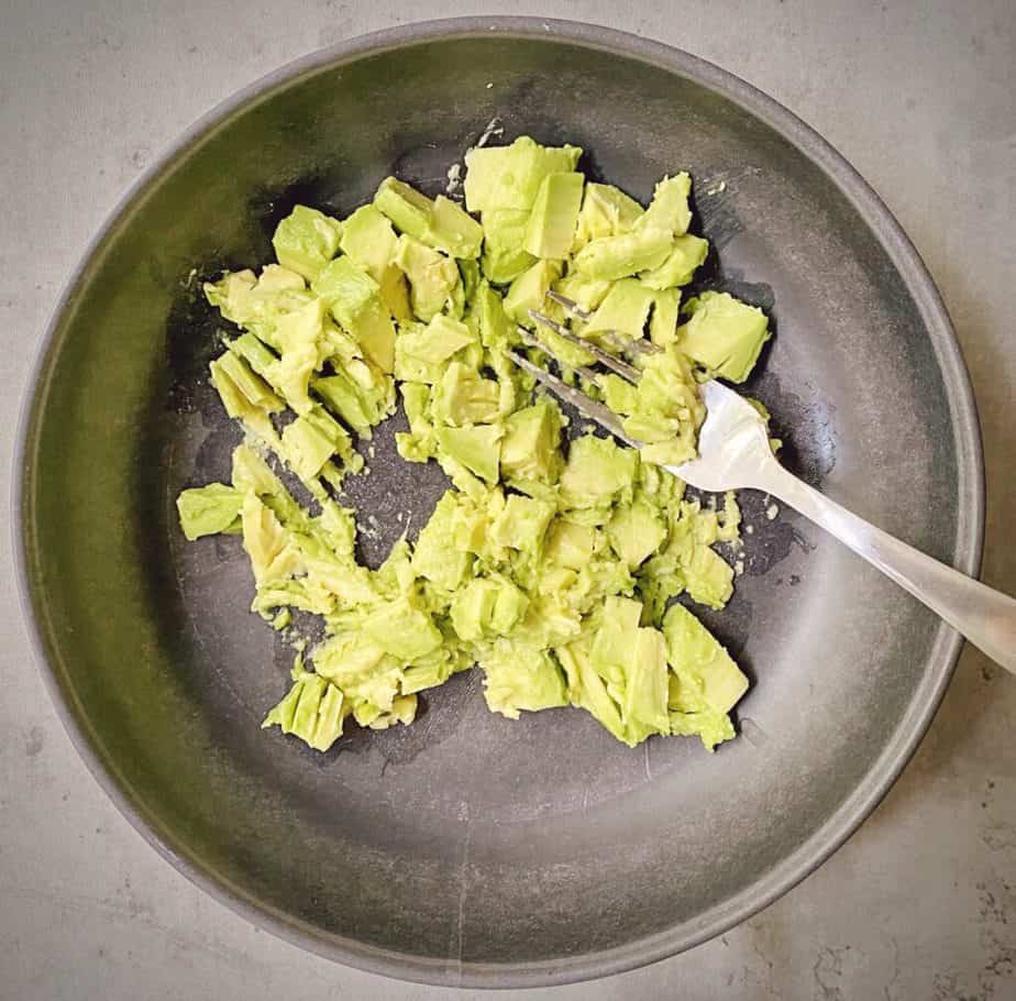 flat lay shot of avocados being mashed in a grey pasta bowl. 