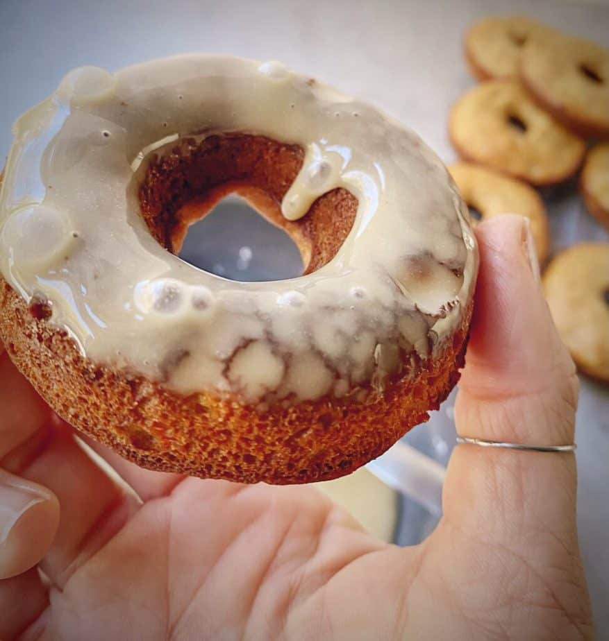 hand holding banana walnut donut after dipping in glaze and letting it drip off.