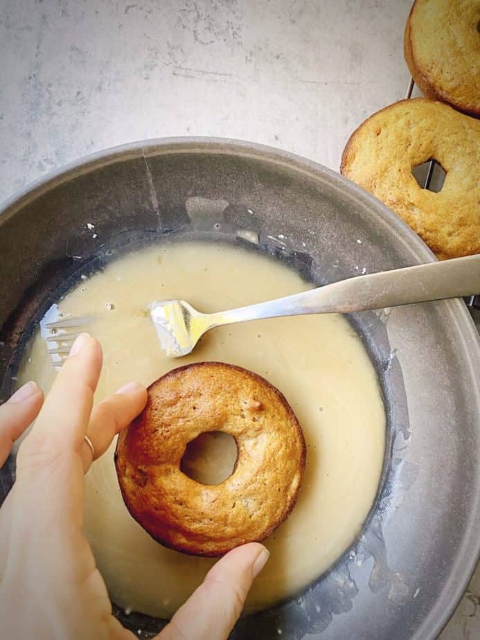 dipping baked banana bread donut in maple glaze.