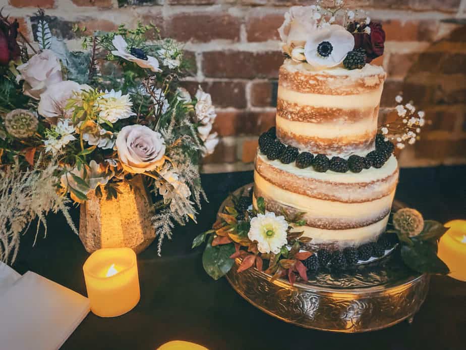 horizontal shot of diy wedding cake on a table next to a beautiful arrangement of flowers and small candles.