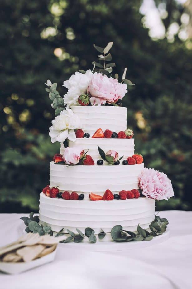 fully frosted 4 tier cake with berries and flowers.