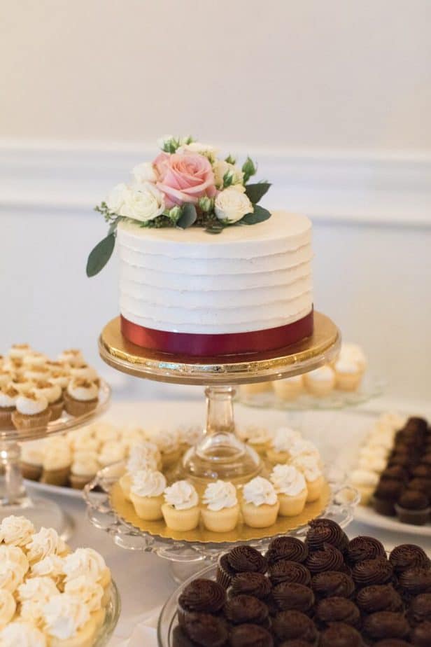 small wedding cake on a cake stand surrounded by other smaller treats as a dessert bar.