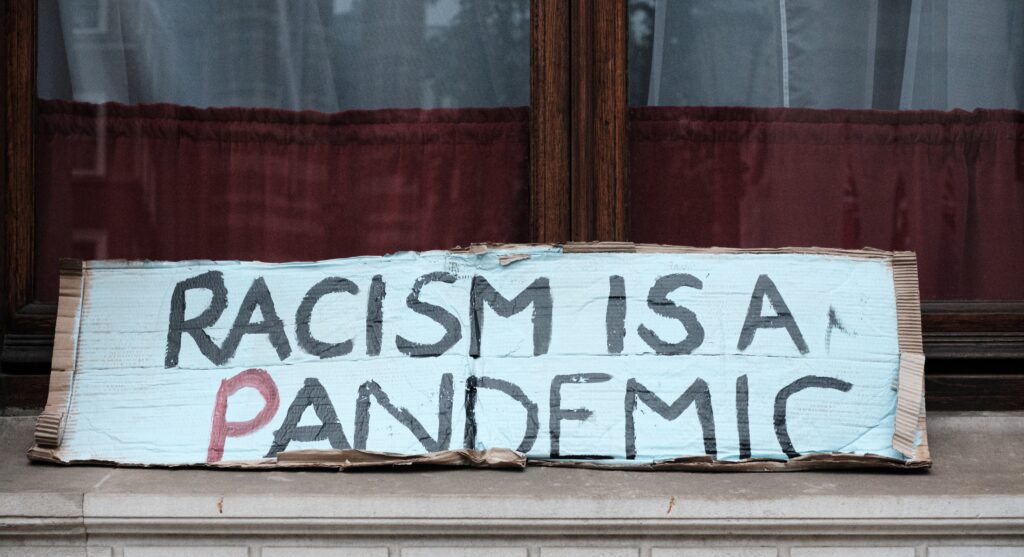 cardboard sign in front of a building that reads "racism is a pandemic."