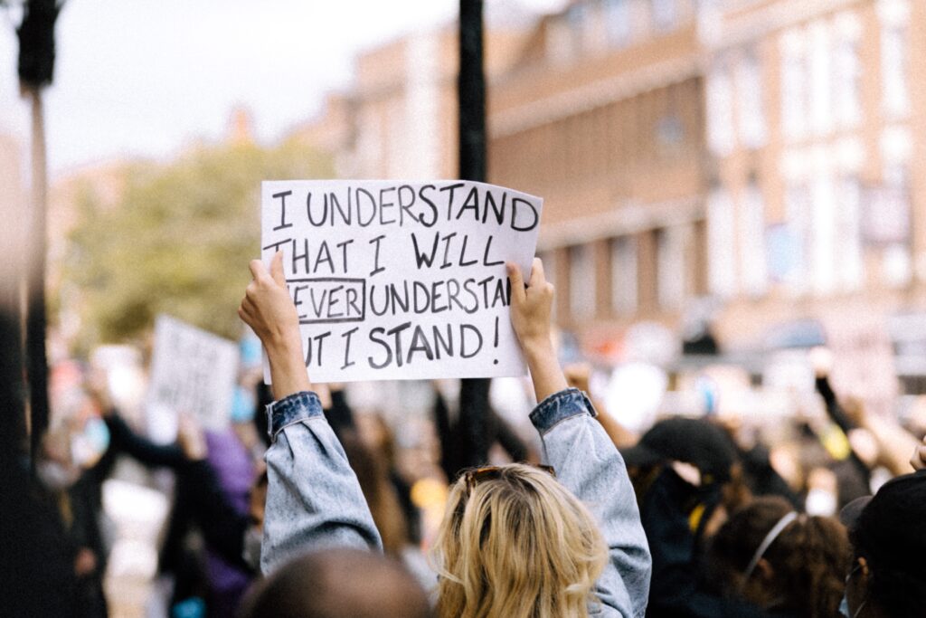 white woman holding sign that says "I understand that I will never understand and yet I stand."