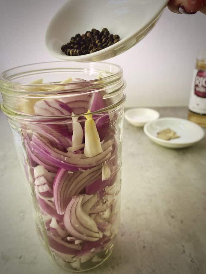 adding peppercorn to jar with red onions.