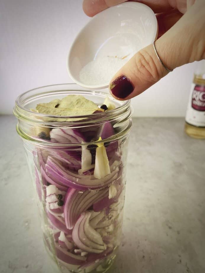 adding sugar to jar with red onions for pickling.