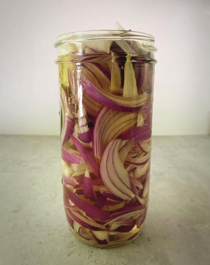 jar of red onion pickles is filled with vinegar.