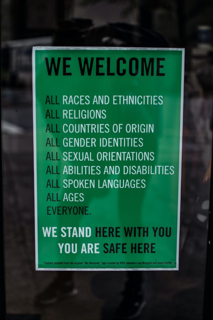 green sign on store door that reads " we welcome all races and ethnicities, all religions, all countries of origin, all gender identities, all sexual orientations, all abilities and disabilities, all spoken languages, all ages, everyone. We stand here with you, you are safe here."