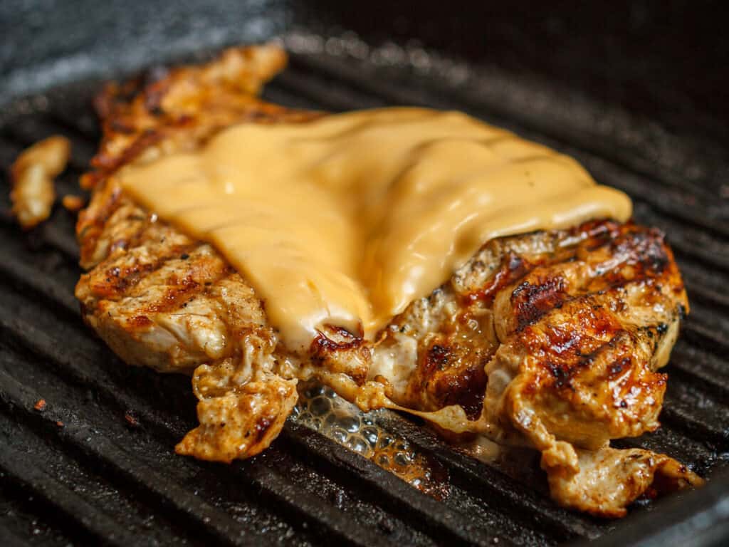 chicken cooking on the grill with a slice of american cheese melting on top.