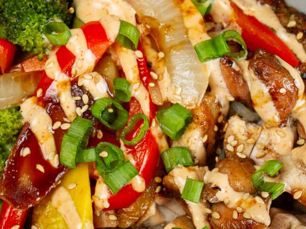 very closeup shot of hibachi chicken and veggies topped with yum yum and scallions.