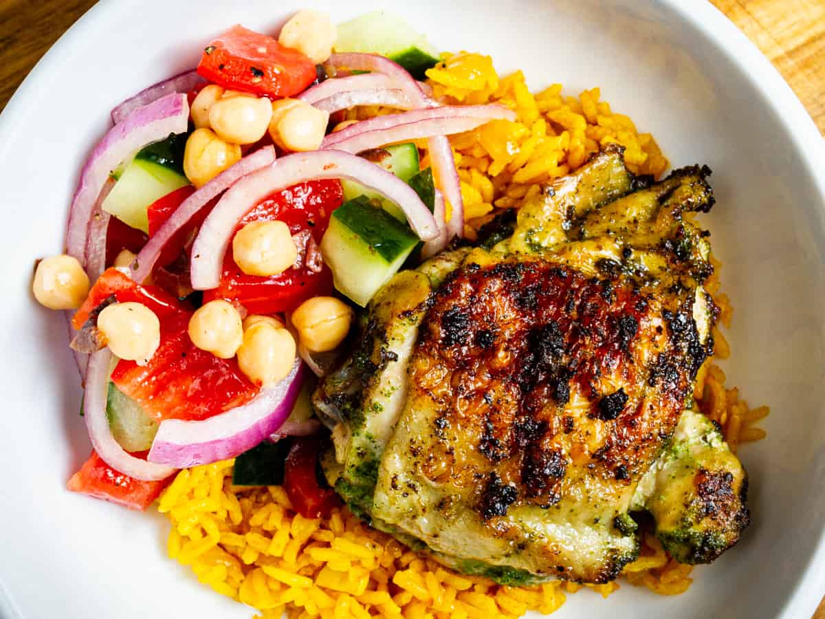 zhoug chicken thigh on a bed of turmeric rice with a side of Mediterranean chopped salad.