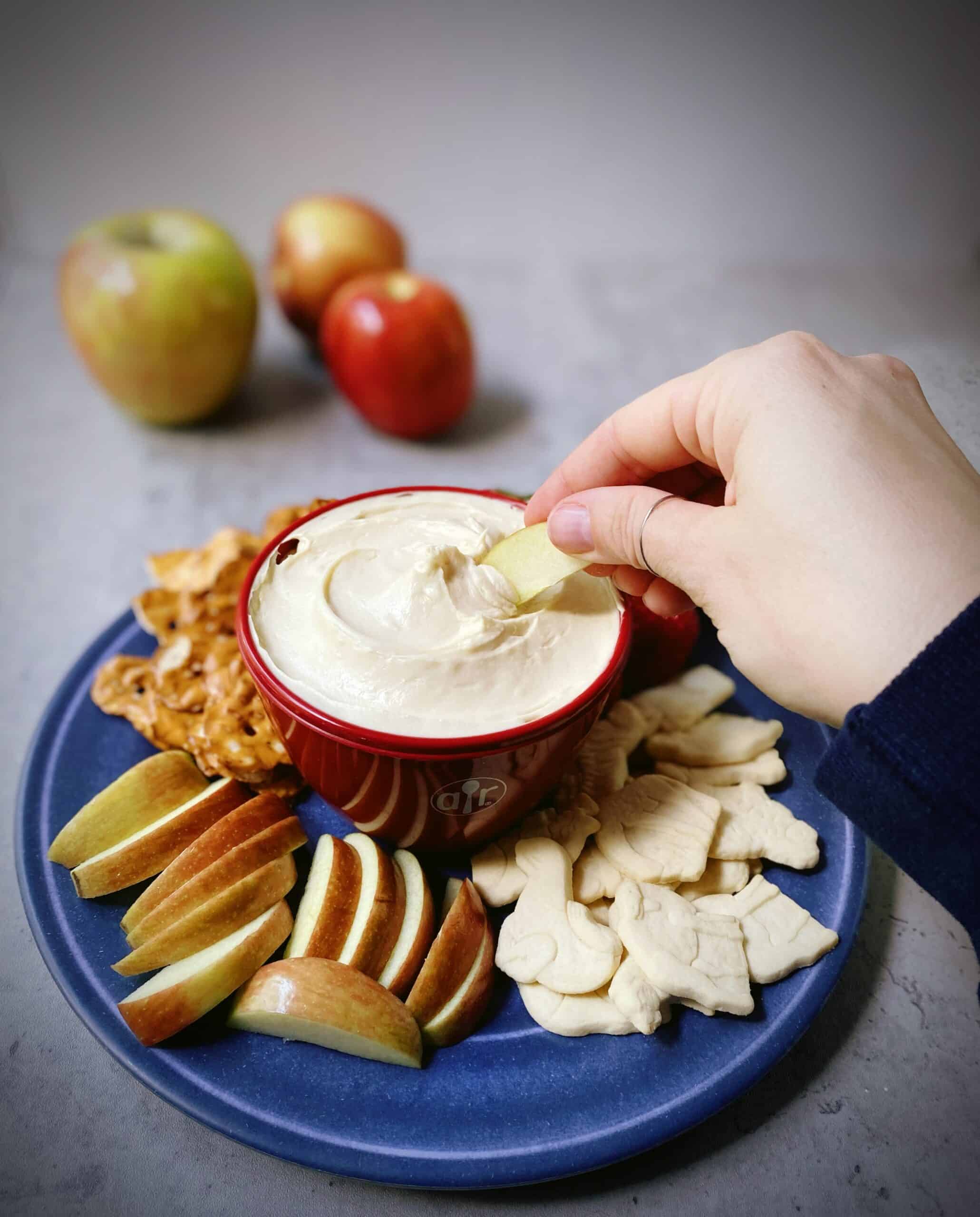 hand dipping an apple in the cream cheesecake dip.
