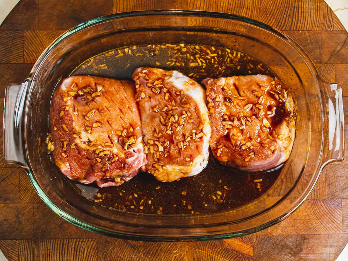 pork chops in a glass dish after being topped with pineapple teriyaki hawaiian marinade.