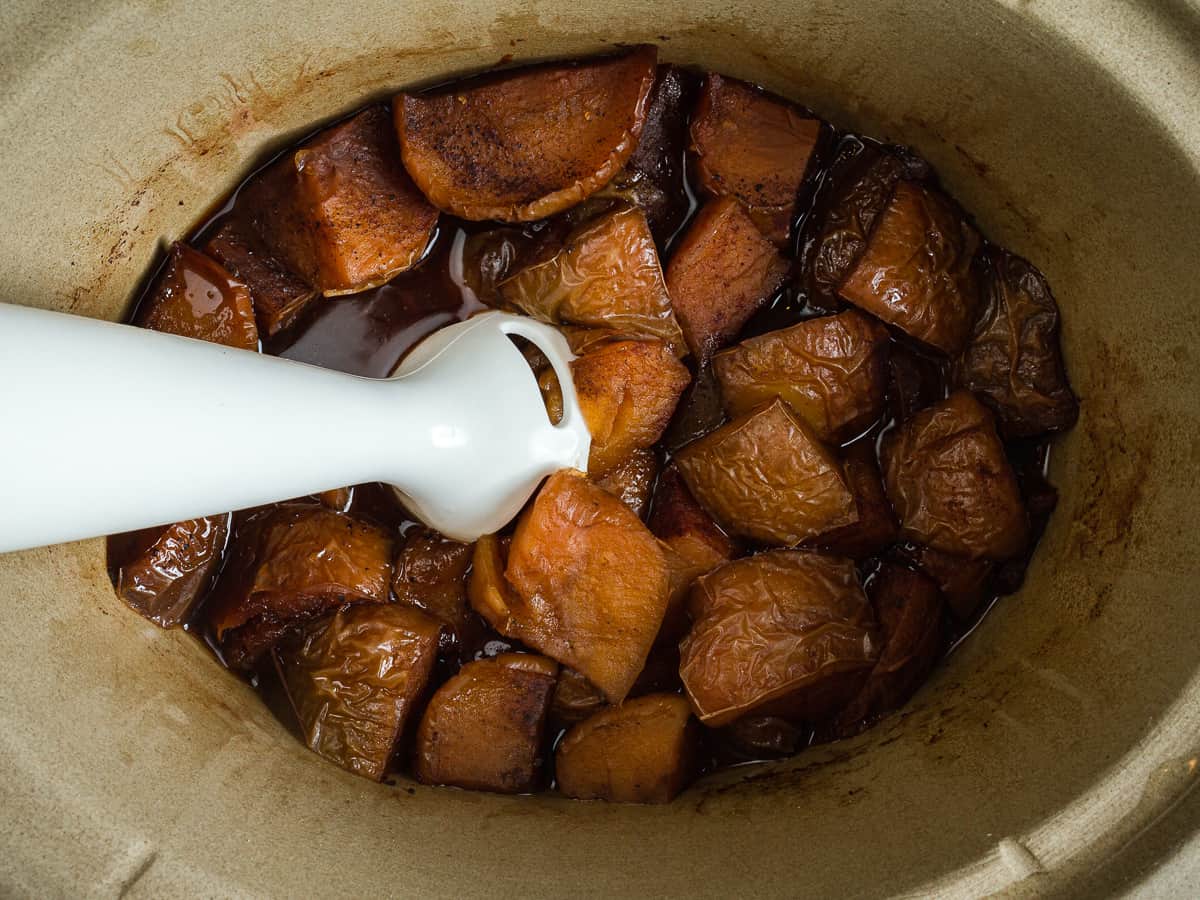 using an immersion blender to blend apples into apple butter.