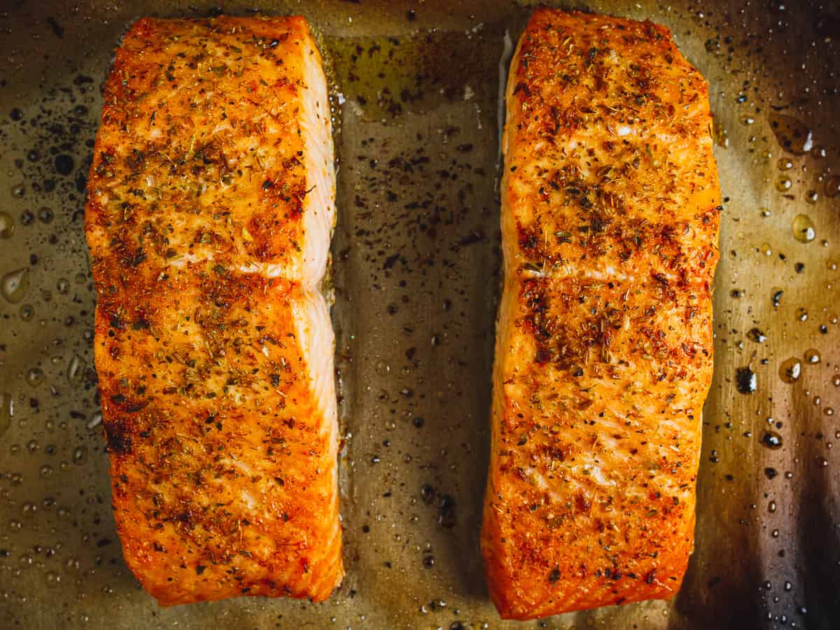 charbroiled salmon fillets on a parchment lined sheet tray.