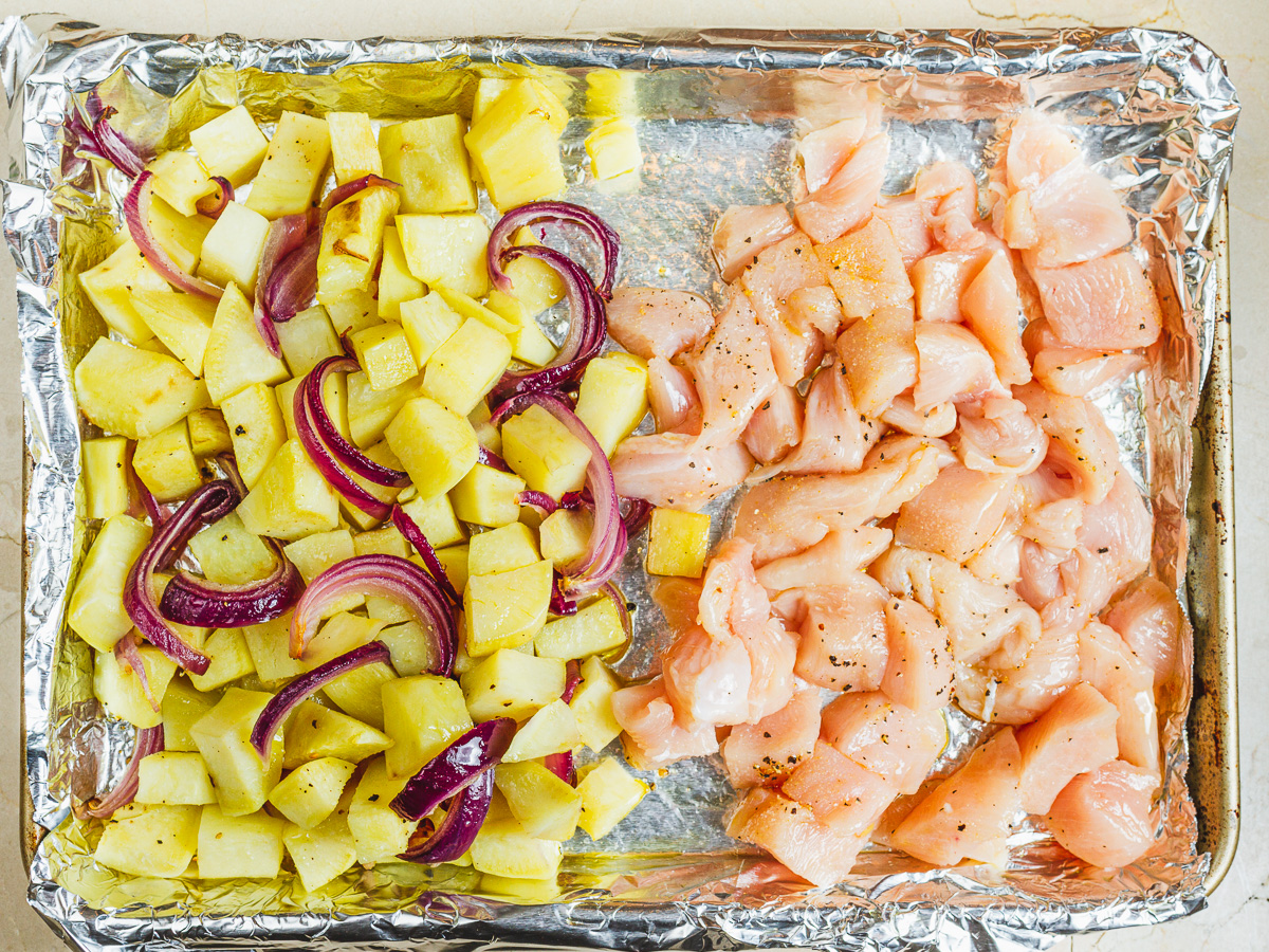 sweet potatoes and onions pushed to one side of the sheet pan to make room for the seasoned chicken breast cubes.