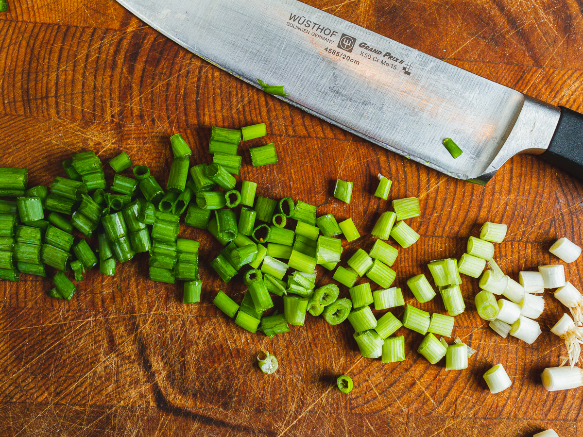 thinly sliced green onions on a cutting board next to a chef's knife.