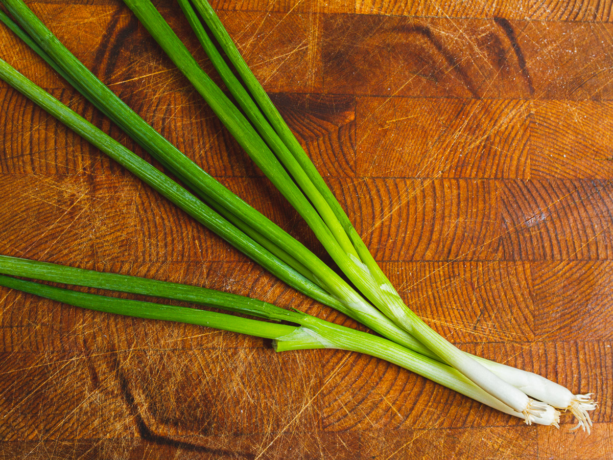3 green onions on a wooden cutting board.